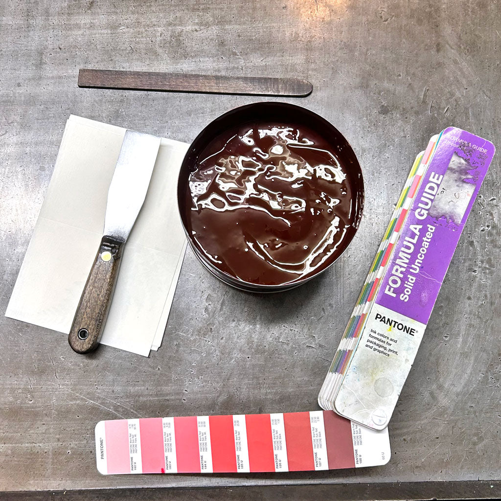 A tin of freshly mixed red ink beside a palette knife and Pantone formula guides