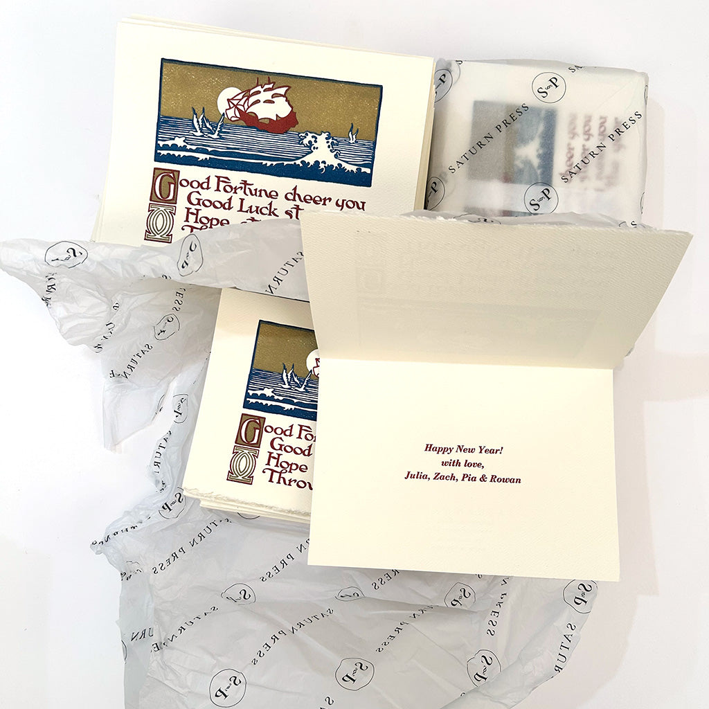 Finished Good Fortune cards, one open to its hand-set red New Year&rsquo;s greeting, nested in Saturn Press tissue